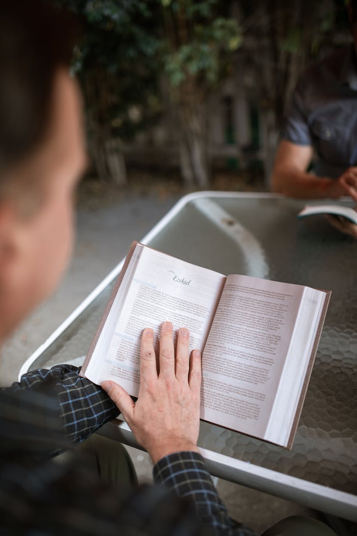 A man intently reading a Bible at an outdoor table, fostering a moment of spirituality and reflection.